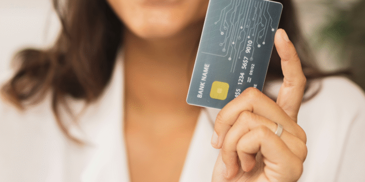 Mulher sorrindo segura cartão de crédito moderno com chip dourado, close nas mãos.