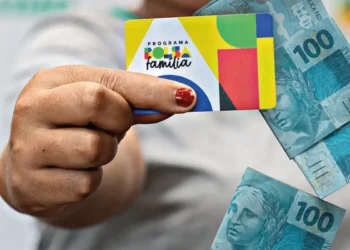 Cartão do programa Bolsa Família 2025 com cédulas de R$ 100 ao fundo, representando a ajuda financeira de R$ 600 por mês