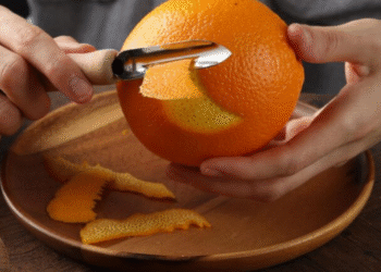 Descascando uma laranja com um utensílio de cozinha, representando o uso de cascas de laranja para aromatizar armários.