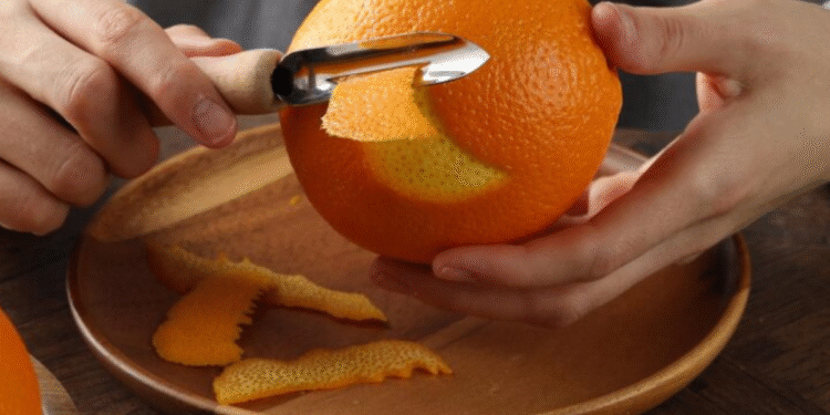 Descascando uma laranja com um utensílio de cozinha, representando o uso de cascas de laranja para aromatizar armários.