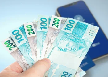 Cédulas de R$ 100 e R$ 200 ao lado da Carteira de Trabalho Digital.