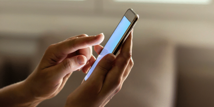 Mãos segurando smartphone enquanto navegam na tela em ambiente interno.