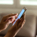 Mãos segurando smartphone enquanto navegam na tela em ambiente interno.