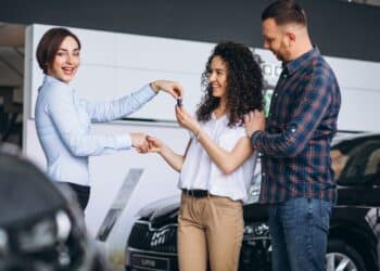 Casal recebe a chave do carro novo de uma vendedora, representando a decisão de compra de um veículo à vista ou parcelado.