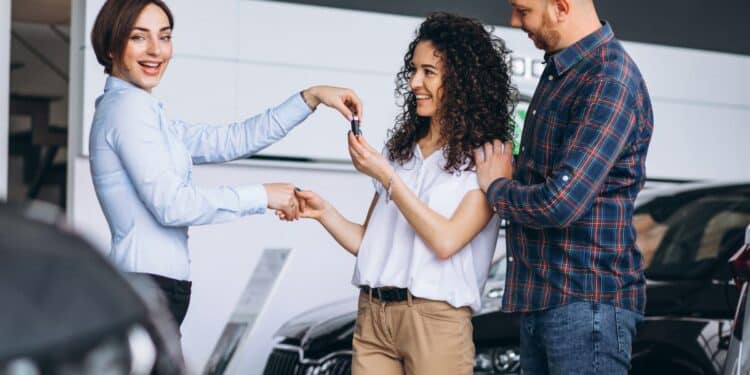 Casal recebe a chave do carro novo de uma vendedora, representando a decisão de compra de um veículo à vista ou parcelado.