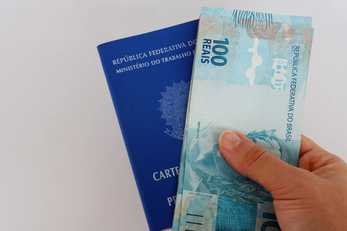 Antigo PIS/Pasep Carteira de Trabalho e cédula de 100 reais brasileiros sendo segurados por uma mão