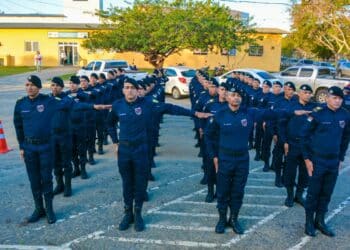 Grupo de guardas municipais alinhados fazendo treinamento em pátio externo.
