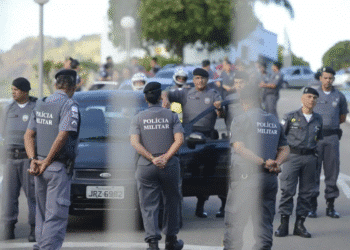 Policiais militares em operação cercando um carro preto em uma rua no Brasil.
