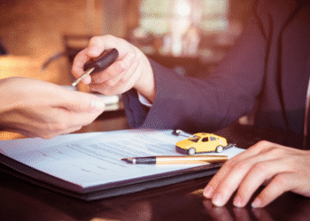 Pessoa entregando chave de carro a outra após assinar contrato e miniatura de carro amarelo.
