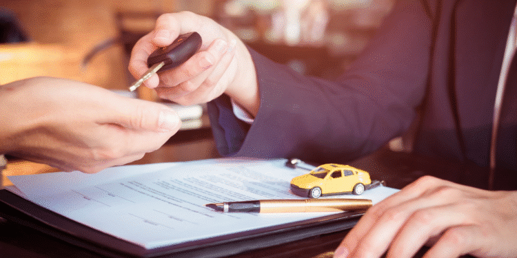 Pessoa entregando chave de carro a outra após assinar contrato e miniatura de carro amarelo.