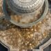 Moedas de cor amarela e prateada acumuladas no fundo de uma fonte de pedra, com a água escorrendo.
