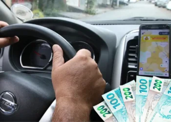 Motorista de Uber segurando o volante enquanto dirige, com notas de dinheiro em destaque