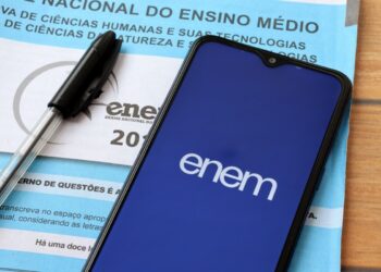 Celular exibindo logo do ENEM sobre prova e caneta preta.