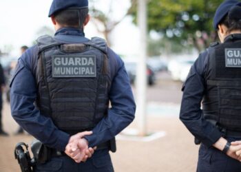 Guardas municipais de costas durante patrulhamento em área urbana.