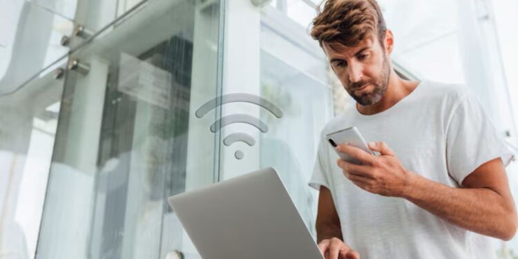 Homem verificando celular e notebook para identificar acesso indevido ao Wi-Fi