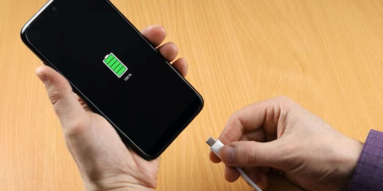 Mãos segurando um celular sendo carregado, indicando bateria cheia.