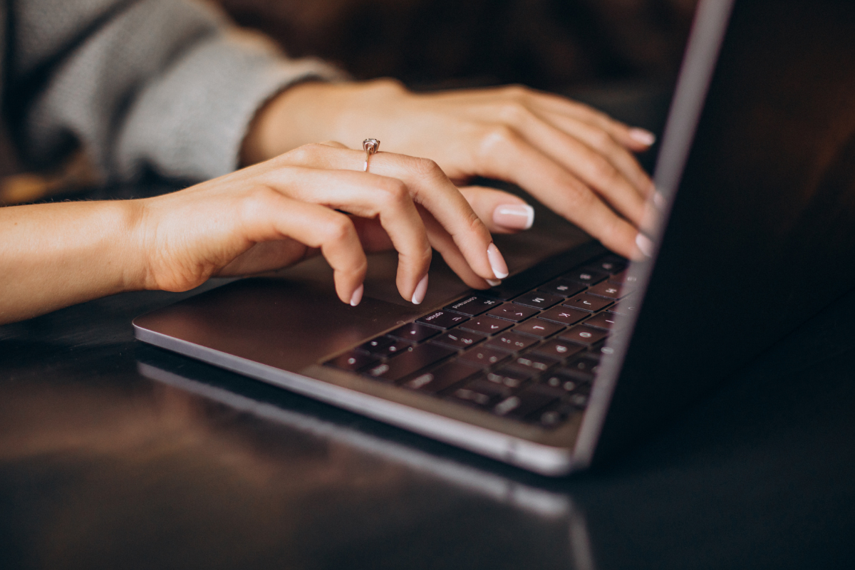 Mãos de mulher com unhas bem feitas digitando em teclado de notebook.