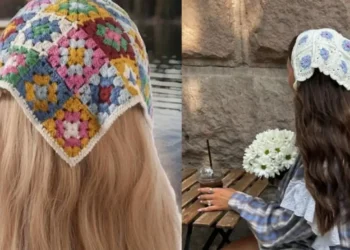 Mulher de costas, em um cenário à beira de um lago, usando um lenço de crochê azul com um padrão de flores brancas.