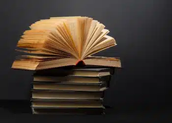 Livros empilhados com um exemplar aberto no topo, simbolizando a leitura e a vasta jornada de conhecimento para a prova de literatura.