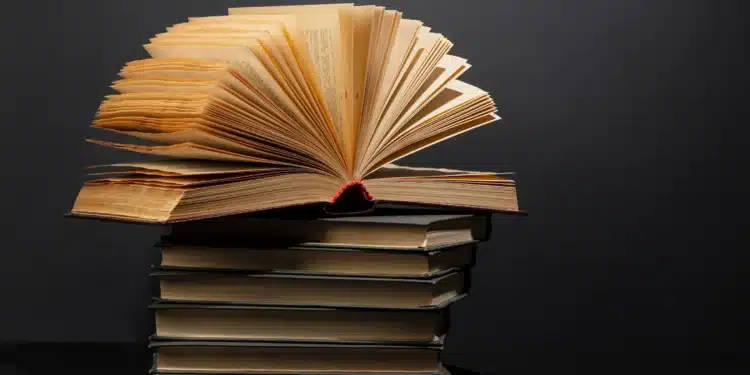 Livros empilhados com um exemplar aberto no topo, simbolizando a leitura e a vasta jornada de conhecimento para a prova de literatura.