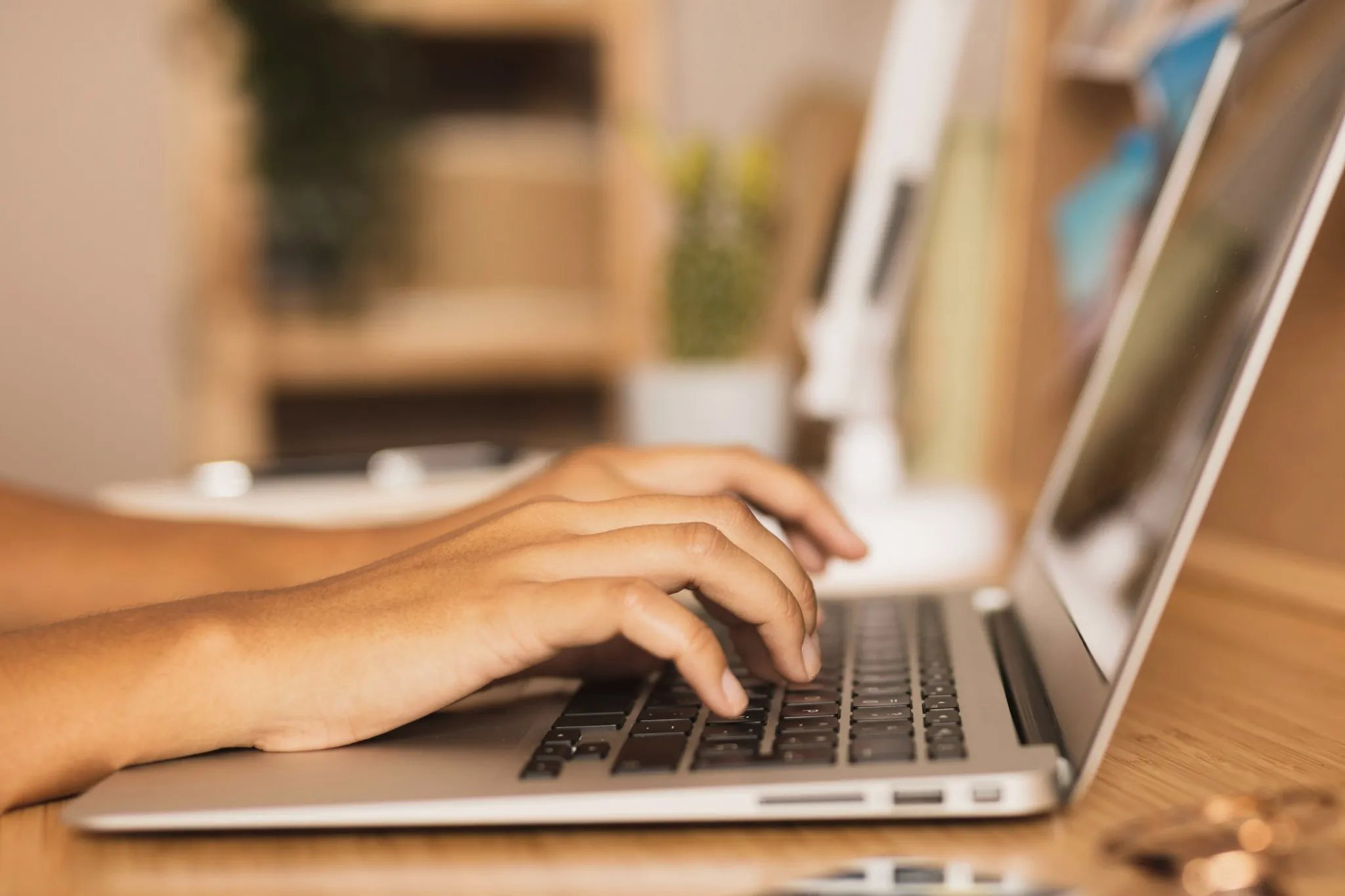 Concurso Prefeitura Mãos digitando em laptop prateado vistas de lado.