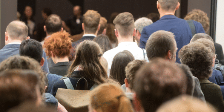 Grupo de pessoas visto de costas participando de um evento ou conferência em ambiente fechado