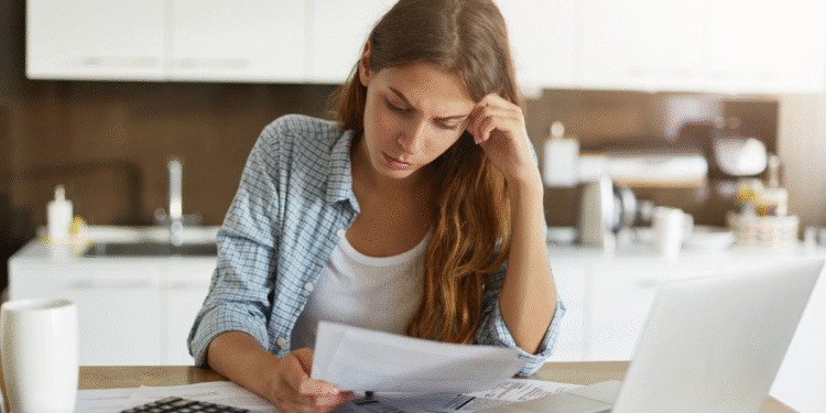 Mulher preocupada analisando contas e usando calculadora na cozinha.