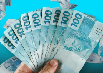 Mão segurando várias notas de 100 reais em leque sobre fundo azul