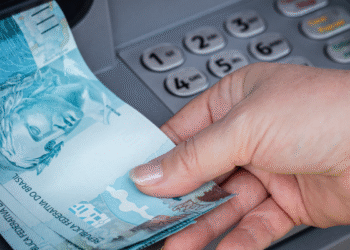 Mão retirando notas de cem reais de caixa eletrônico no Brasil.