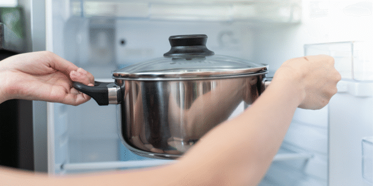 Pessoa colocando uma panela de inox com tampa na geladeira aberta.
