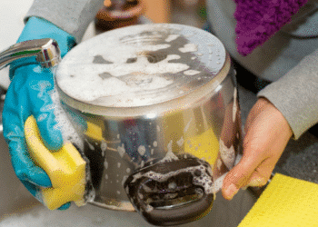 Pessoa usando luva azul lava panela inox com esponja amarela e sabão.