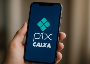 Mão segurando smartphone com aplicativo PIX da CAIXA aberto na tela, mostrando logo verde sobre fundo azul