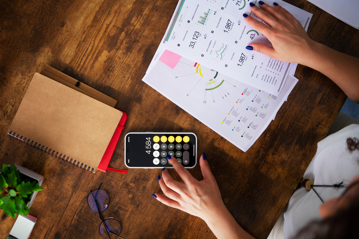 Planejamento financeiro Mulher calculando dados financeiros com planilhas e calculadora no celular sobre mesa de madeira.