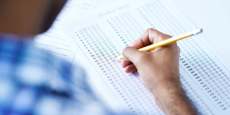Pessoa revisando a chave de respostas de um exame, com lápis, indicando o processo de revisão para garantir acertos.