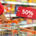 Pessoa empurrando carrinho de compras com etiqueta de 50% de desconto no supermercado