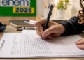 Estudante treinando redação do Enem 2026 com folha de prova e caneta sobre a mesa de estudos.