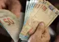Pessoa segurando cédulas de real em dinheiro, representando o saque de R$ 6.220 do FGTS disponível para solicitação até 27 de julho.