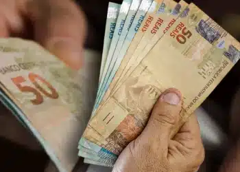 Pessoa segurando cédulas de real em dinheiro, representando o saque de R$ 6.220 do FGTS disponível para solicitação até 27 de julho.