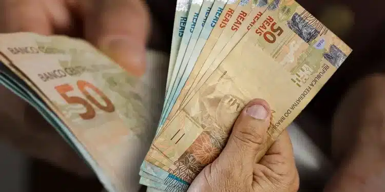 Pessoa segurando cédulas de real em dinheiro, representando o saque de R$ 6.220 do FGTS disponível para solicitação até 27 de julho.