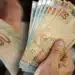 Pessoa segurando cédulas de real em dinheiro, representando o saque de R$ 6.220 do FGTS disponível para solicitação até 27 de julho.