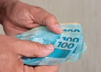 Mãos segurando notas de real representam o pedido do Saque Calamidade do FGTS de até R$ 6.220, disponível até domingo, 2 de agosto.
