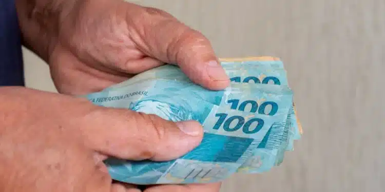 Mãos segurando notas de real representam o pedido do Saque Calamidade do FGTS de até R$ 6.220, disponível até domingo, 2 de agosto.