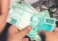 Pessoa segurando cédulas de real representando a solicitação do saque de R$ 6.220 do FGTS para moradores de cidades em situação de calamidade.