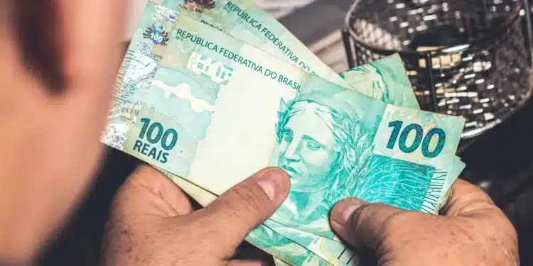 Pessoa segurando cédulas de real representando a solicitação do saque de R$ 6.220 do FGTS para moradores de cidades em situação de calamidade.