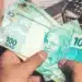 Pessoa segurando cédulas de real representando a solicitação do saque de R$ 6.220 do FGTS para moradores de cidades em situação de calamidade.