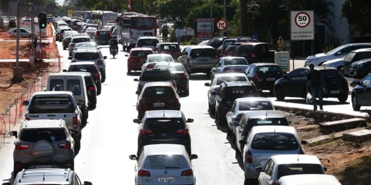 Trânsito pesado em uma rua com várias faixas e carros estacionados ao longo do meio-fio, representando a circulação de veículos na cidade.