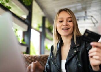 Jovem sorridente com cartão preto premium usando laptop em ambiente moderno