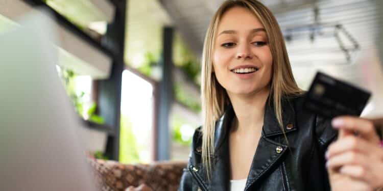 Jovem sorridente com cartão preto premium usando laptop em ambiente moderno