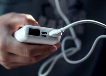 Pessoa segurando power bank prata com múltiplas portas USB-C conectado a cabo branco em ambiente veicular