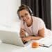 Mulher estudando de casa com notebook, fones de ouvido e anotações, representando a carreira de educador on-line.